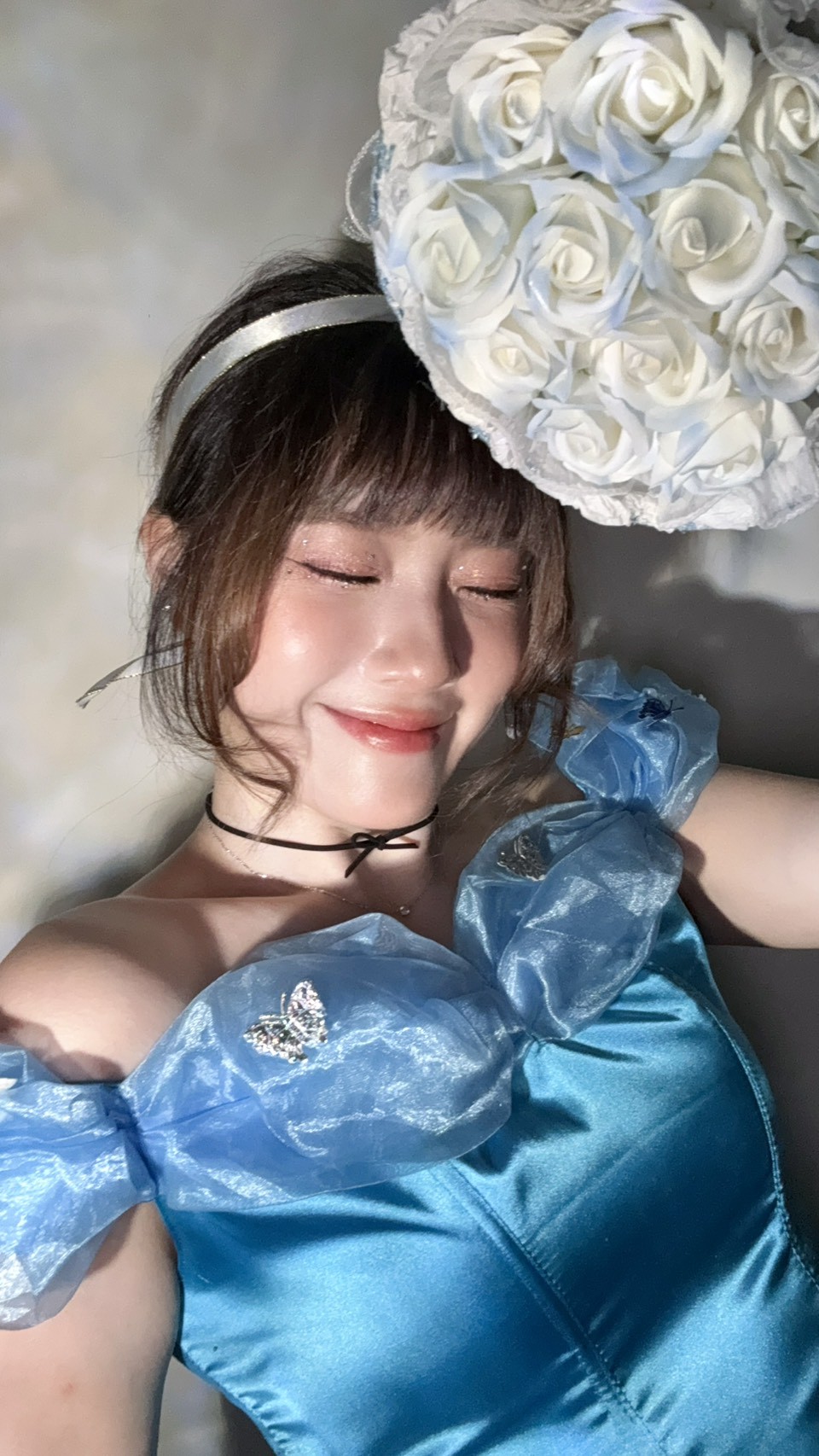 麥莉穿著藍色禮服,閉眼微笑並舉起白玫瑰花束